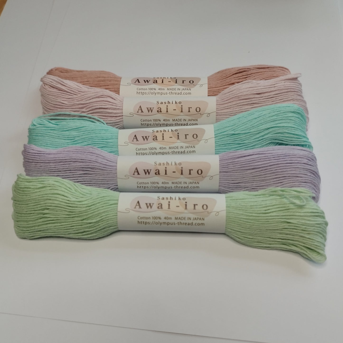 Several skeins of Olympus Sashiko Awai-iro thread in pastel colors neatly arranged on a white surface.