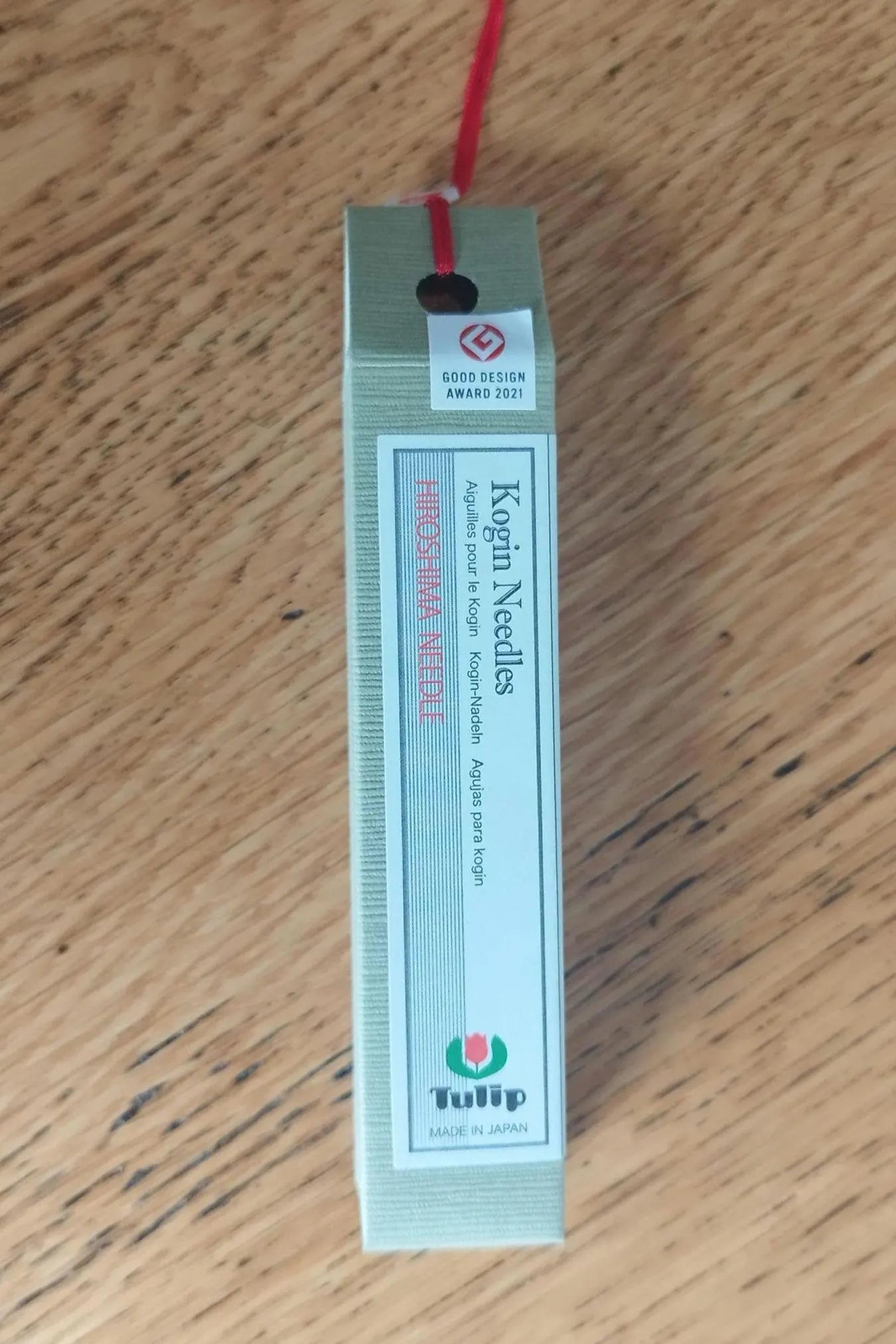A package of Tulip Kogin needles with a red thread attached, placed on a wooden surface.