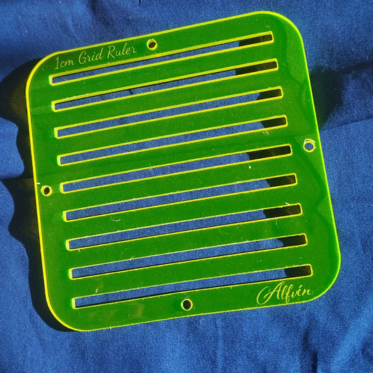 A translucent yellow acrylic grid ruler with 1cm spacing, engraved with '1cm Grid Ruler' and the brand 'Alfven'. It has holes on the side for alignment.