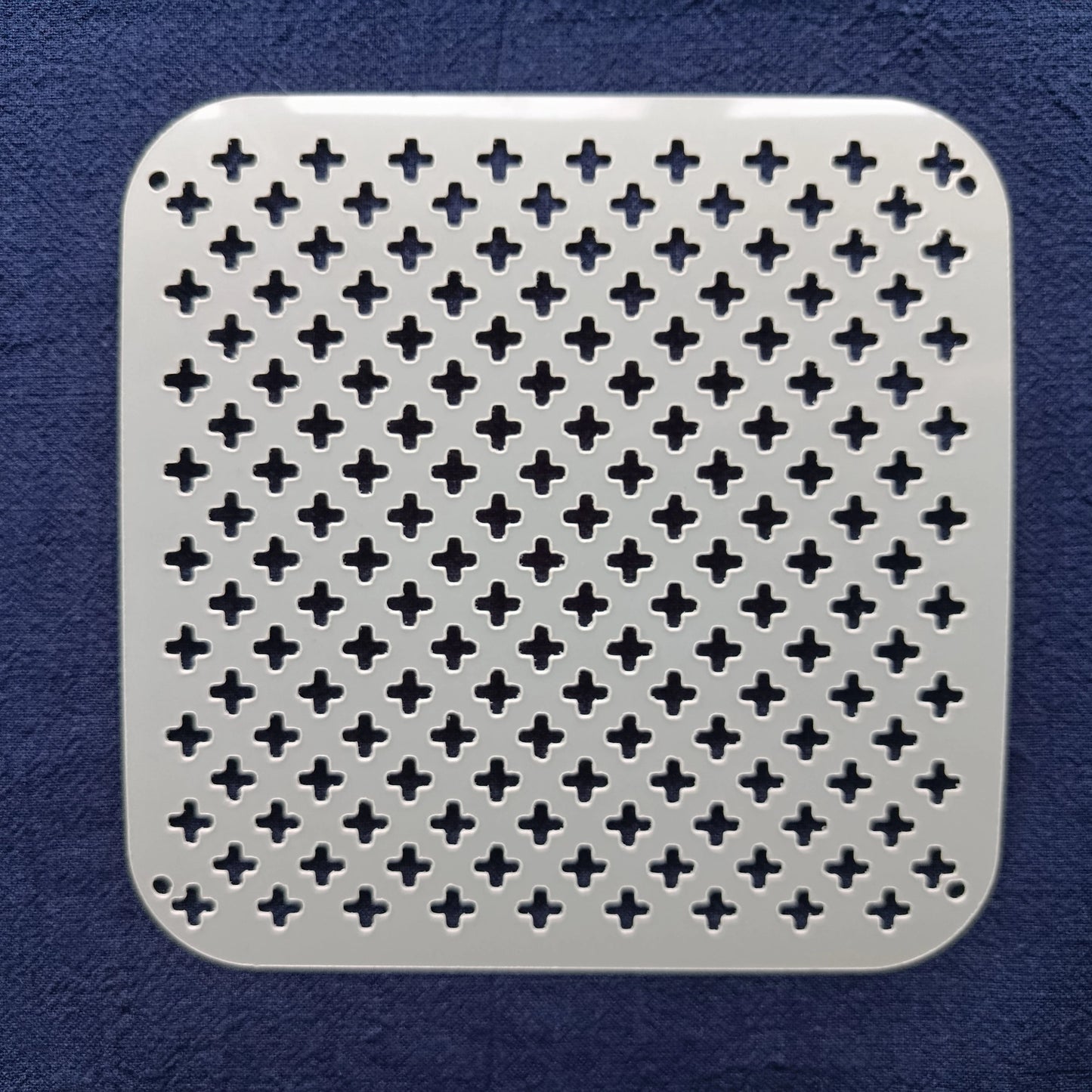 white square stencil of alternating crosses on a blue fabric background