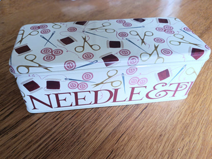 Decorative tin box with needle and thread design on a wooden surface
