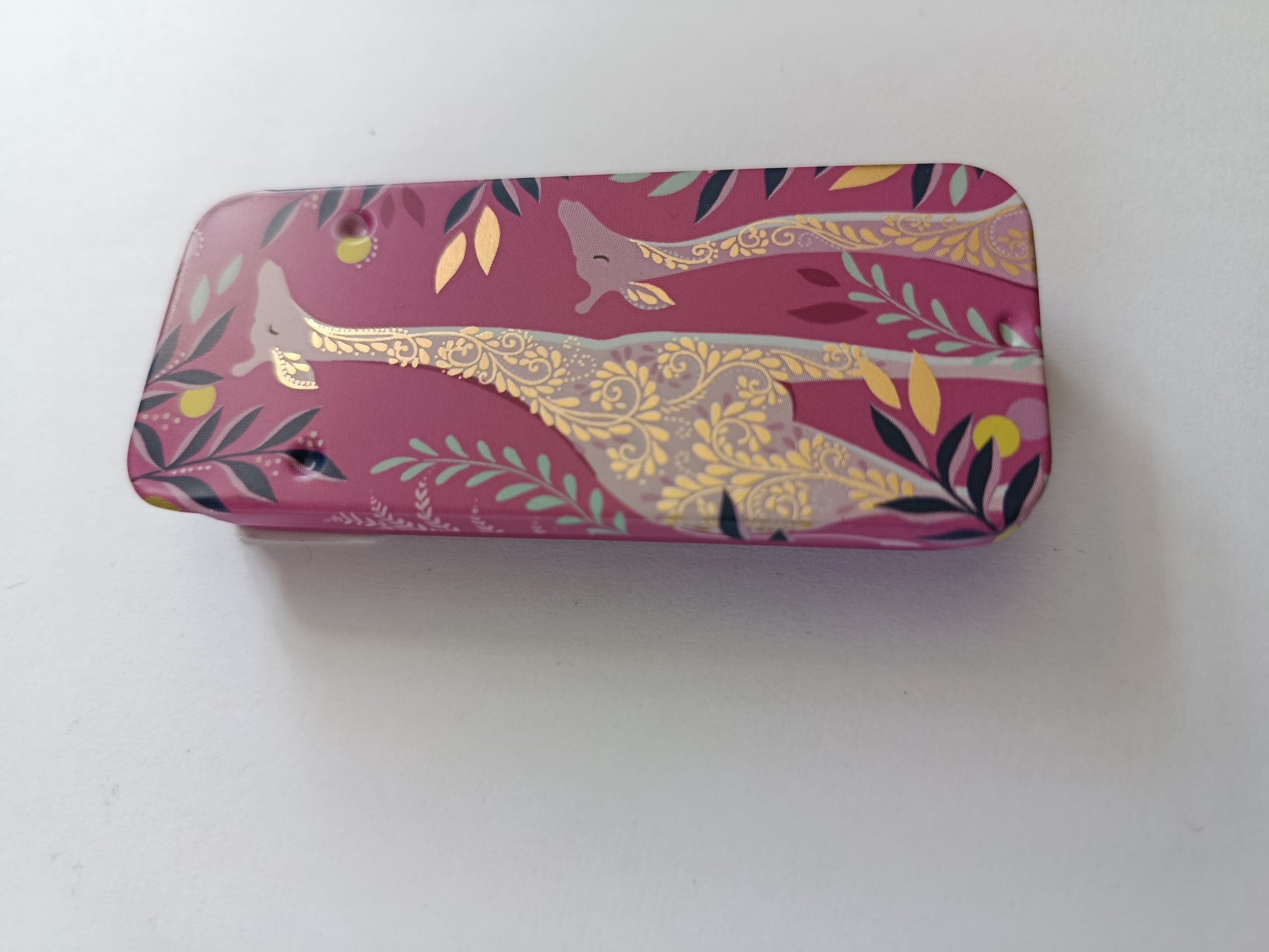 Pink and gold patterned giraffes on a metal needle storage tin on a white background