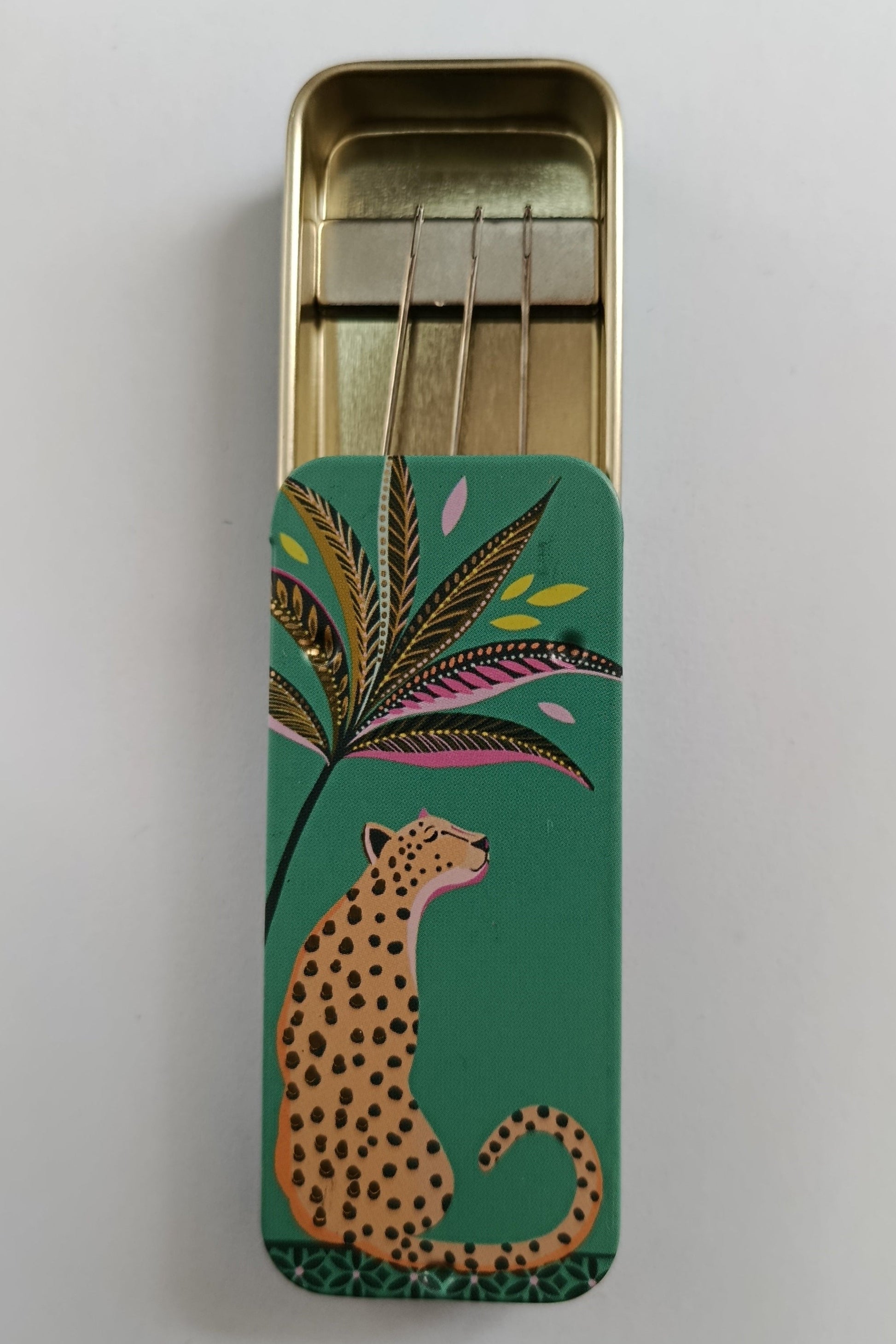 Small rectangular tin with a leopard and leaf design on a green background containing magnet to hold sewing needles in place