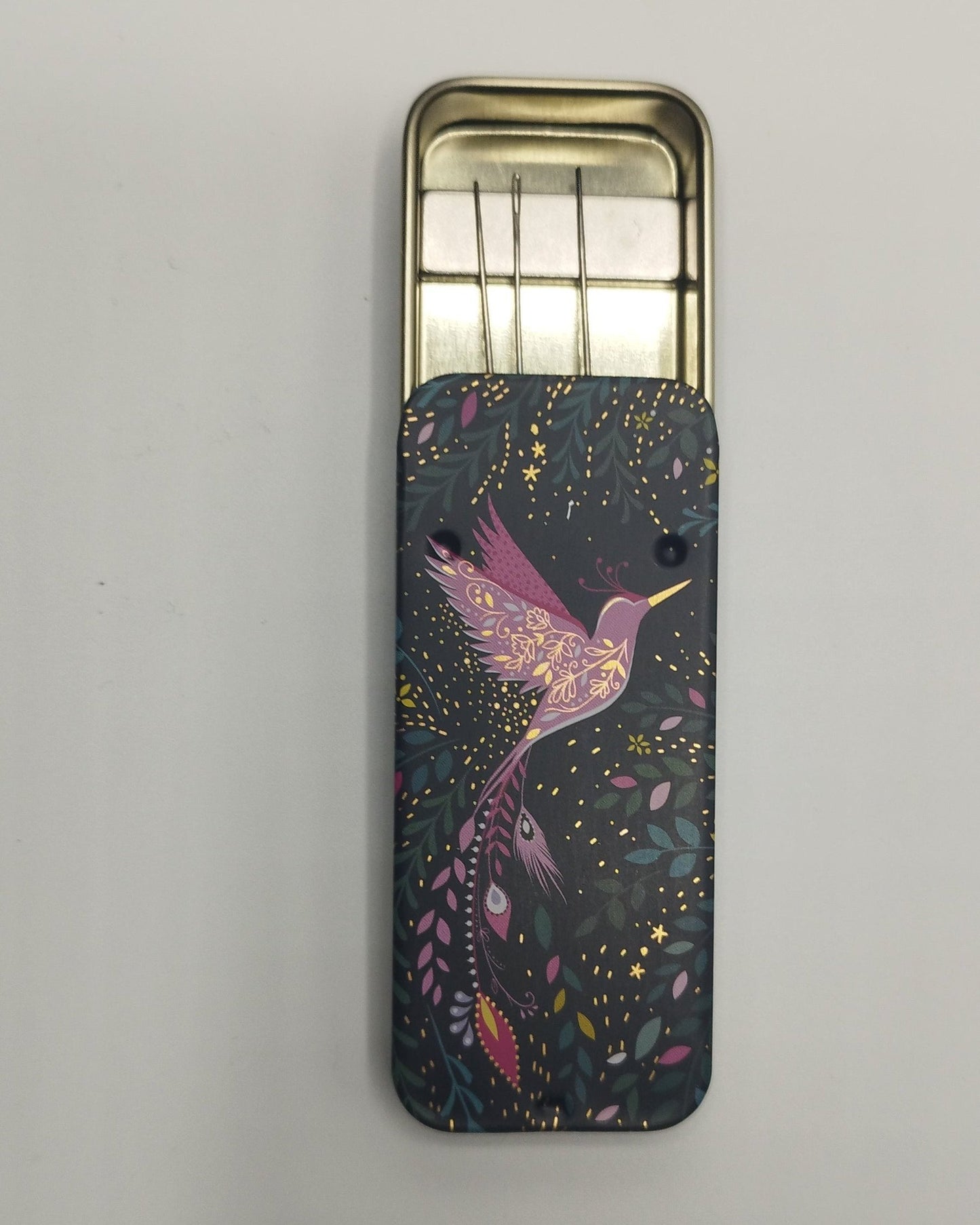 Open Slider tin containing a magnet holding the needles in place. Tin as a dark floral background with a pink flying hummingbird on it
