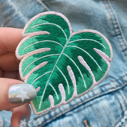 Green embroidered leaf patch held over a denim background