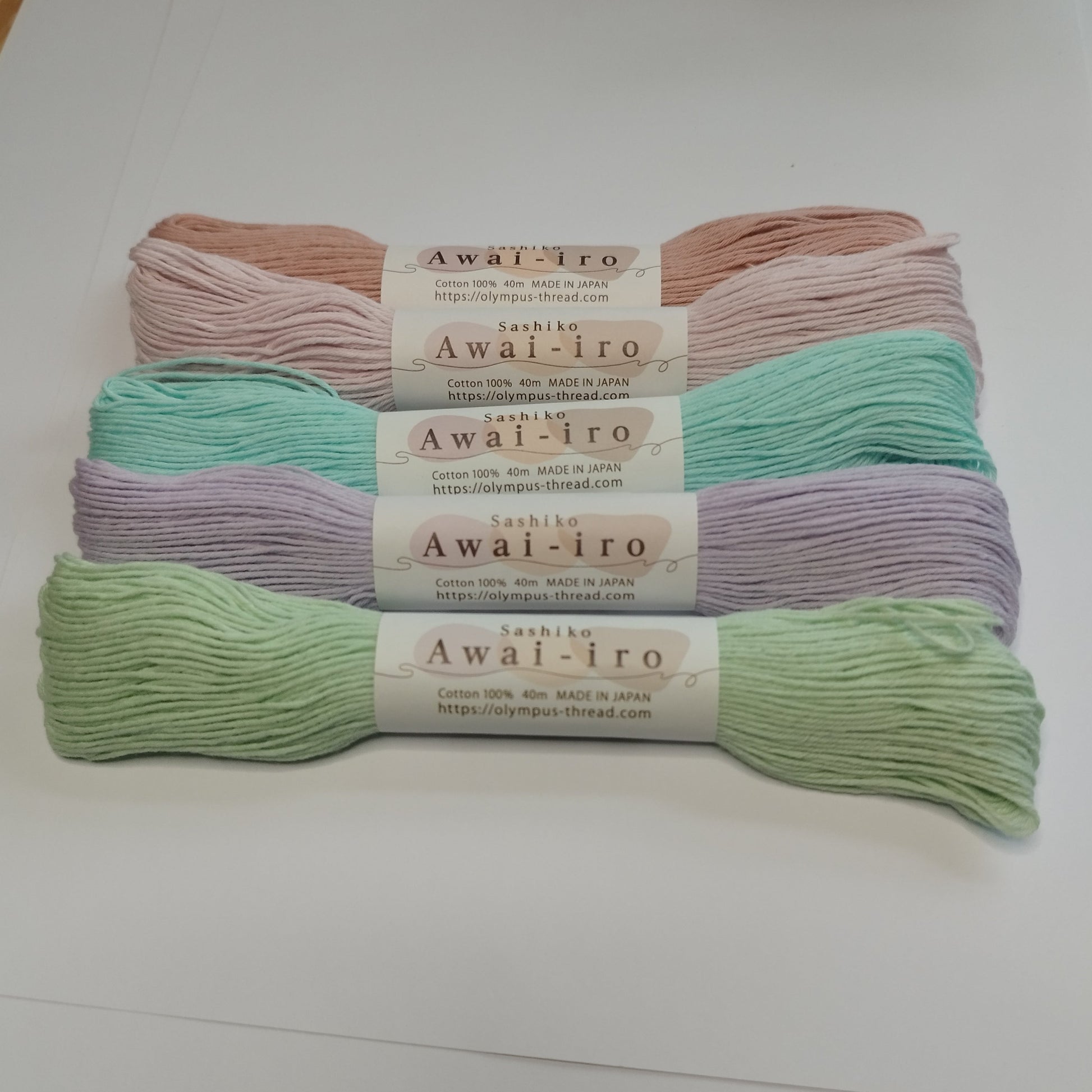 Several skeins of Olympus Sashiko Awai-iro thread in pastel colors neatly arranged on a white surface.