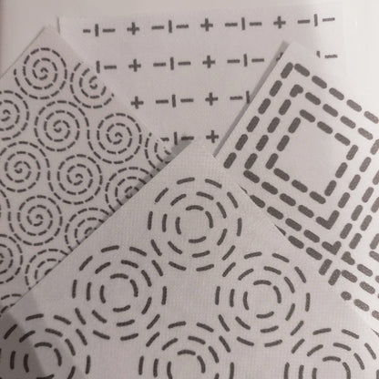 4 Sashiko Transfers. In the foreground is a concentric circles pattern. On the right is a concentric square pattern. At the back is a crosses and dashes sashiko pattern. On the left is a swirls dashed sashiko pattern