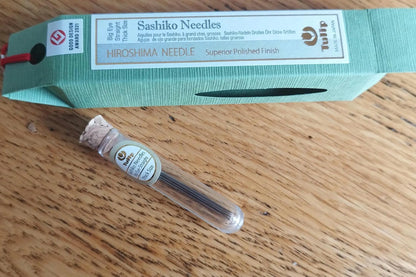 A package of Tulip Hiroshima sashiko needles with one needle displayed in front of the packaging, showing a thick needle with a large eye designed for embroidery.