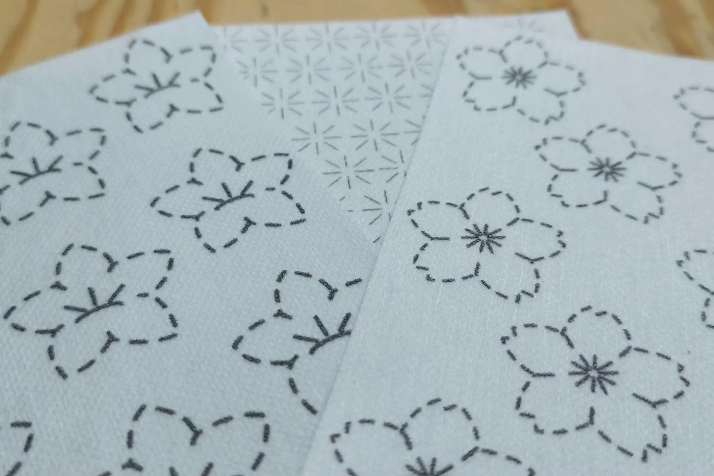 Two sheets of washable paper with floral embroidery patterns on a wooden surface