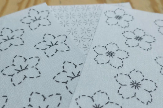 Two sheets of washable paper with floral embroidery patterns on a wooden surface