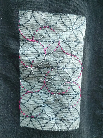 Rectangular Sashiko Design of overlapping circles, on black denim.  Design is partially stitched through with pink and white variegated thread. 