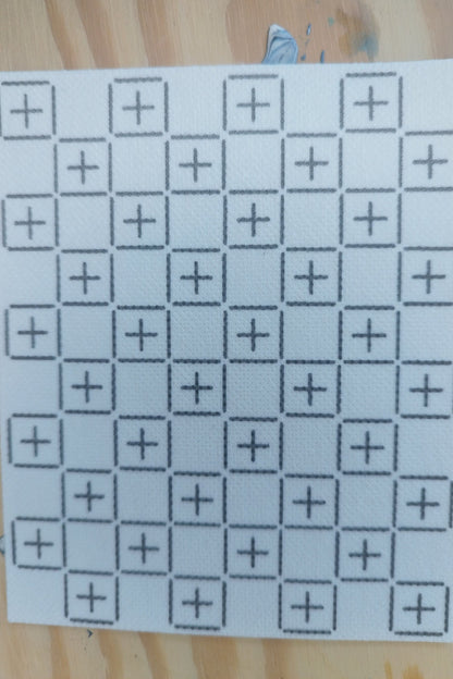Rectangular sashiko design of alternating boxes containing a cross, with a gap in between each one. The design is 4 boxes wide, and 5 boxes tall. On a light wood background.